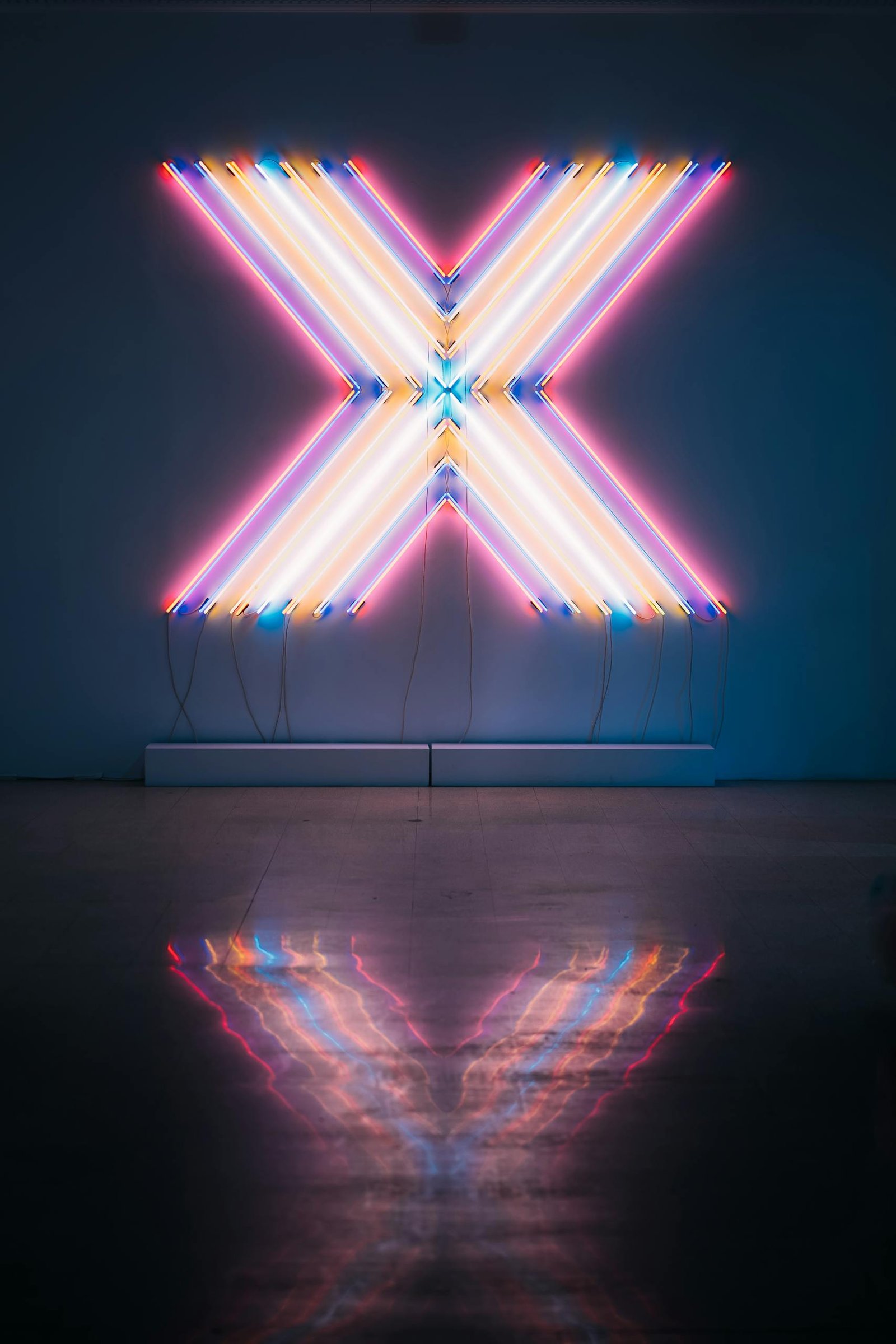 Vibrant neon X sign with colorful reflections on a dark floor background.